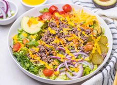 a salad with meat, cheese and onions in a white bowl on a striped towel