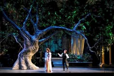 two people are standing on stage in front of a tree and some stairs at night