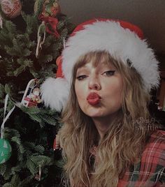 a woman wearing a santa claus hat blowing out her tongue in front of a christmas tree