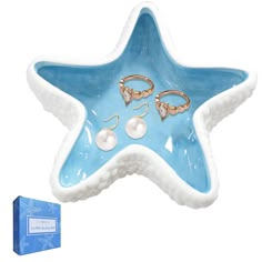 a blue starfish shaped dish with two pairs of earrings on it next to a box