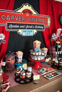 a table topped with cakes and cupcakes next to a red curtain