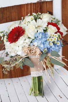 a bridal bouquet with red, white and blue flowers on a wooden chair in front of a door