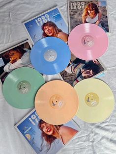 four different colored vinyl records are laying on a white sheet and there is an album in the middle