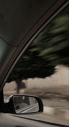 the rear view mirror of a car as it drives down a street with trees in the background