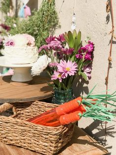 some carrots and flowers are sitting on a table next to a basket with cake