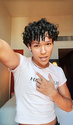 a man with curly hair wearing a white shirt and holding his hand up to the side