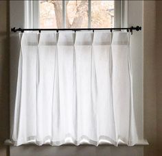 a window with white curtains and a tree in the distance behind it on a sunny day