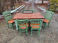 a wooden table and four green chairs sitting on top of a gravel road covered in snow