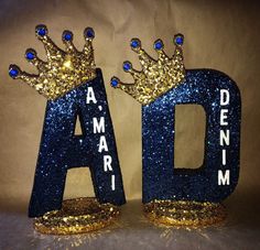 two blue and gold glitter letters with crowns on each letter are shown in front of a brown background