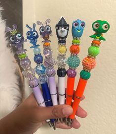 a person holding up a bunch of different colored pens with cartoon characters on them in front of a white wall