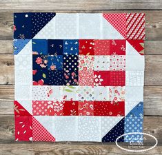 a patchwork quilt with red, white and blue squares on it sitting on a wooden surface