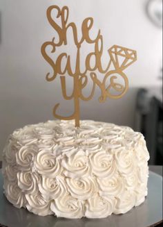 a cake with white frosting and a gold topper that says she said yes