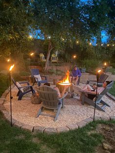 an outdoor fire pit surrounded by lawn chairs and lights with people sitting around it at night