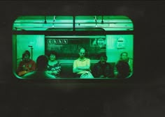 group of people sitting on a subway car in the dark, with green light coming from their windows