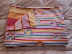 a colorful blanket laying on top of a bed next to an orange and pink pillow