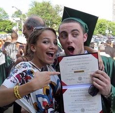 two people in graduation gowns posing for the camera with one holding up a certificate