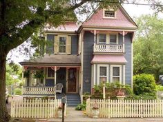 a blue house with a pink roof and white picket fence in front of the house