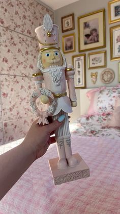 a hand holding a nutcracker figurine on top of a pink bed