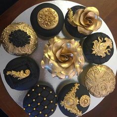 a white plate topped with black and gold decorated cookies next to a golden rose on top of it