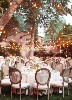 tables and chairs are set up for an outdoor dinner party with fairy lights strung over them