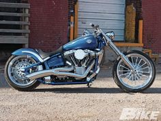 a blue and silver motorcycle parked in front of a red brick building on a dirt road