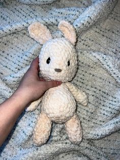 a person holding a small stuffed animal on top of a bed next to a blanket