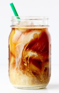 a jar filled with liquid and ice on top of a white table next to a green straw