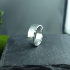 a silver ring sitting on top of a black stone slab next to a green plant