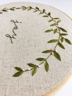 a close up of a embroidery on a piece of cloth with leaves and flowers around it