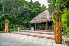 an outdoor seating area with steps leading up to a thatched roof gazebo surrounded by greenery