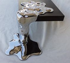 a shiny metal object sitting on top of a black table next to a white wall