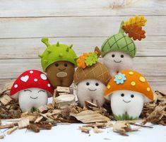 four small stuffed mushrooms sitting on top of dry leaves next to a white wooden wall