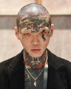 a young man with tattoos on his face and neck is looking at the camera while wearing a black jacket