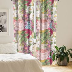 a white bed sitting next to a window covered in pink and green floral print curtains