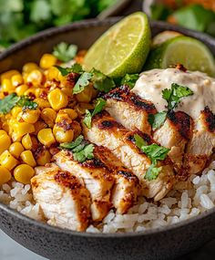 a bowl filled with chicken, rice and corn on top of a table next to lime wedges