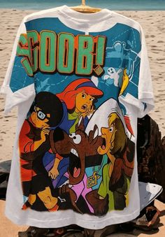 Introducing our white single-stitched overprint t shirt, a must-have for any Scooby-Doo fan! This classic tee combines nostalgic charm with a touch of contemporary style, making it the perfect addition to your casual wardrobe. The front of the shirt showcases the beloved Scooby-Doo gang in their full glory. This delightful illustration captures the essence of the characters, bringing to life the magic of the iconic animated series. From Fred's confident grin to Daphne's elegance, from Velma's in White Themed Cartoon Print T-shirt, Themed White T-shirt With Cartoon Print, White 90s T-shirt With Character Print, Themed White Crew Neck Top, Themed White Top With Graphic Print, Vintage White Top With Cartoon Print, Themed White Graphic Print Top, Vintage White T-shirt With Character Print, Vintage White T-shirt With Cartoon Print