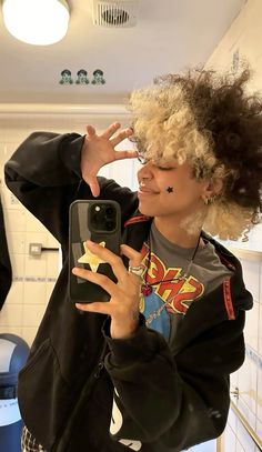 a woman taking a selfie with her cell phone in the kitchen while wearing an afro wig