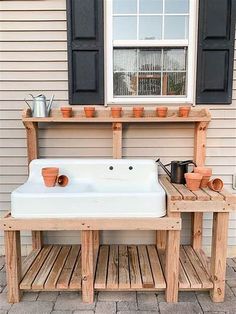 a white sink sitting under a window next to a wooden shelf with pots on it