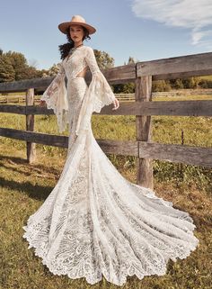 a woman standing in front of a wooden fence wearing a white dress and cowboy hat