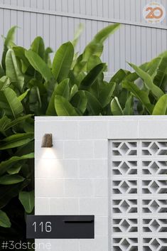 a white brick wall with a light on it and some plants in front of it