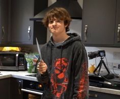 a young man is holding a knife in his hand and smiling at the camera while standing in front of a kitchen counter