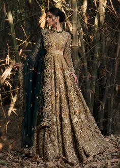 a woman standing in the woods wearing a gold and green gown