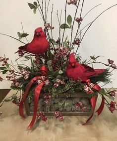 two red birds sitting on top of a wooden box filled with flowers and greenery