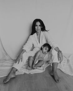 a woman sitting next to a child on top of a white sheeted floor in front of a wall