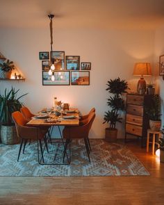 a dining room table set for four with candles on it and potted plants in the corner