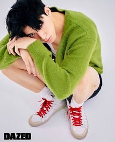 a young man sitting on the ground with his hands under his head and wearing sneakers