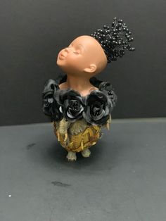 a small figurine with black roses on it's head and hair in the shape of a woman