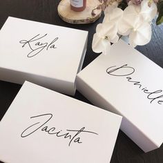 three white boxes with names on them sitting on a table next to flowers and a candle