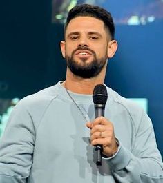 a man holding a microphone in his right hand and wearing a gray sweatshirt on stage