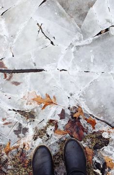 a pair of black shoes sitting on top of an ice covered ground next to leaves